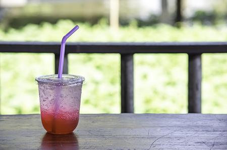 Red juice with ice in a plastic glass on table and river.の写真素材