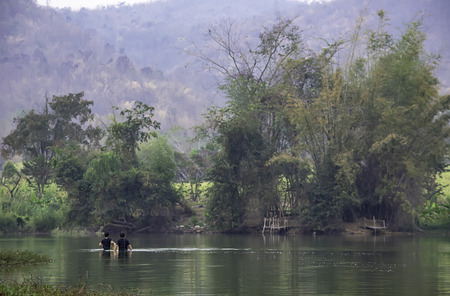 Man holding fishing nets walking in water Background blurred mountains and treesの写真素材