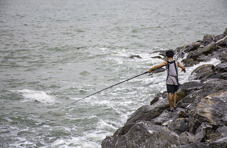 A man holding a fishing rod on the rock by the sea.の写真素材