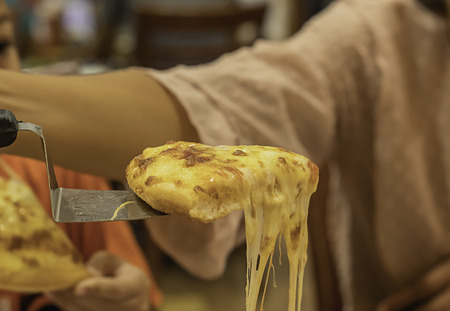 The hand holding Pizza with ham and cheese in spoon from the tray wood.の写真素材