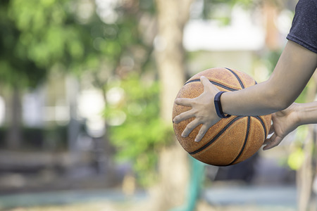 Leather basketball in hand of a woman wearing a watch Background blur tree in park.の写真素材