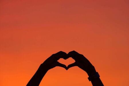 The black silhouette of a heart shaped hands  Background sky orange light of sunset.