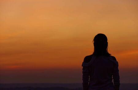The black silhouette of a woman Background sky orange light of sunset.の写真素材