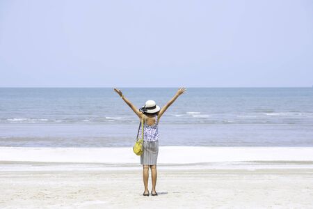 The image behind Asian women raise their arms and wear a hat  background sea.の写真素材