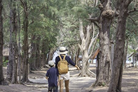 The image behind Mother and son walking Sandwalk road with trees covered Background sea at Phraya Nakhon Cave National Park , Prachuap Khiri Khan , Thailand. March 16, 2020の写真素材