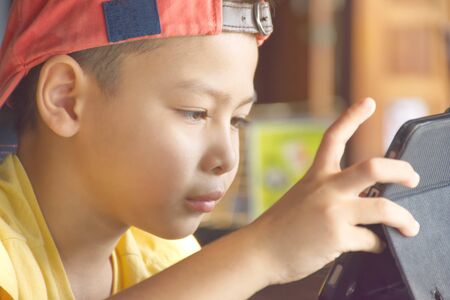 Portrait of Asian boy playing mobile phone on wooden table.の写真素材