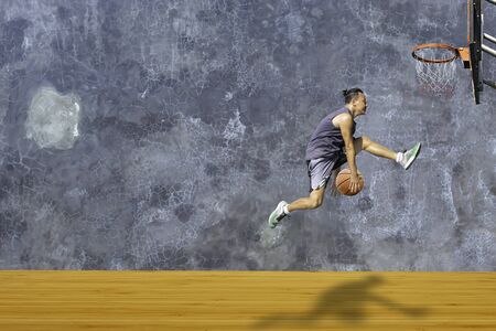 Basketball in hand man jumping Throw a basketball hoop On the wooden floor Background plaster wall loft  with The pattern of cracks.の写真素材