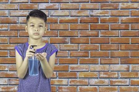 Alcohol gel bottles In the hands of asian boy background brick wall.の写真素材
