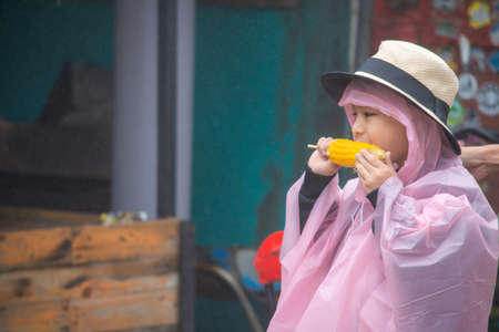 Boy wearing rainwear Eating corn in the hand And rain droplets floating in the air.