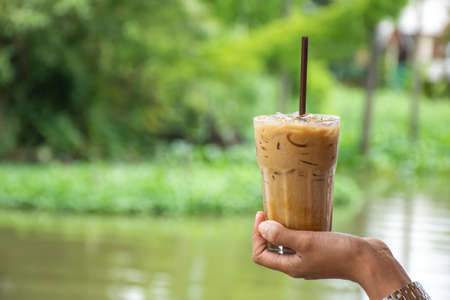 Glass of cold espresso coffee in hand Background blurry views tree and water.の写真素材