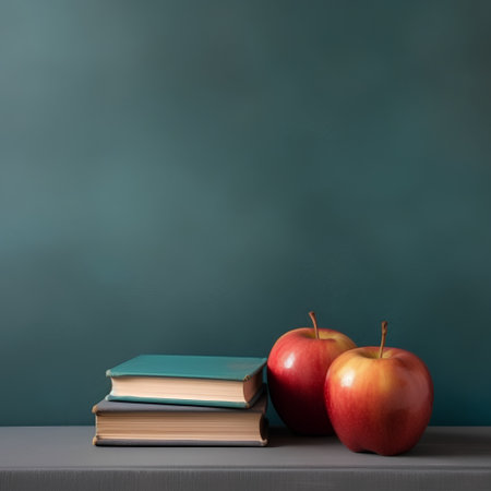 Stack of books and apples on table in front of green chalkboardの素材