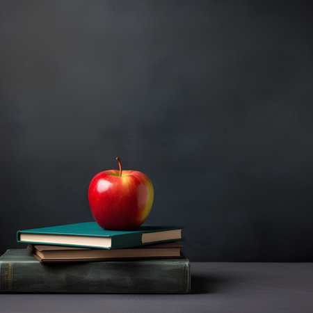 Stack of books and red apple on blackboard background with copy spaceの素材