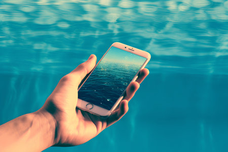 Hand holding mobile phone with seascape on screen over sea backgroundの素材