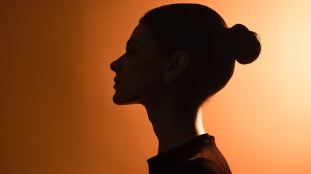 Silhouette of a young beautiful woman on an orange background.の素材