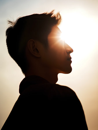 Profile of a young asian man looking at the sun at sunsetの素材