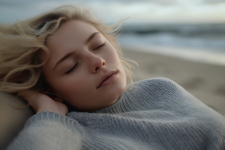 Beautiful young woman sleeping on the beach in a knitted sweaterの素材