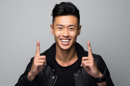 Portrait of a young asian man laughing and pointing up over grey backgroundの素材
