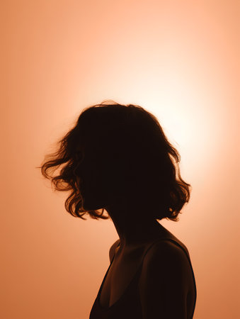 Silhouette of a woman with flowing hair on an orange backgroundの素材
