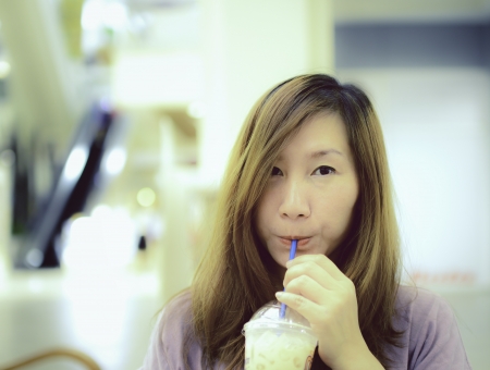 Beautiful Asian woman drinking coffee.. Image is cross-processed giving retro style. の写真素材