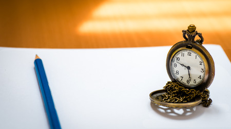 Open blank notebook with blue pencil and pocket watch on  wood background with natural light.の写真素材