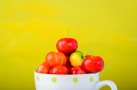 Cherries in cup on wooden table and yellow wall.の写真素材