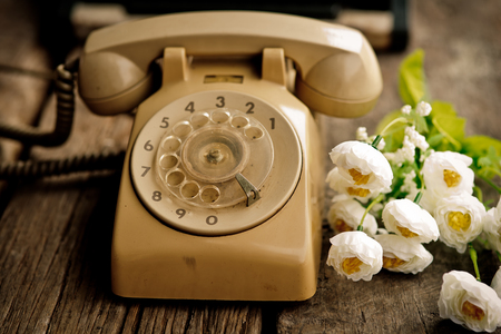 Old vintage telephone with flower on wooden table.の写真素材
