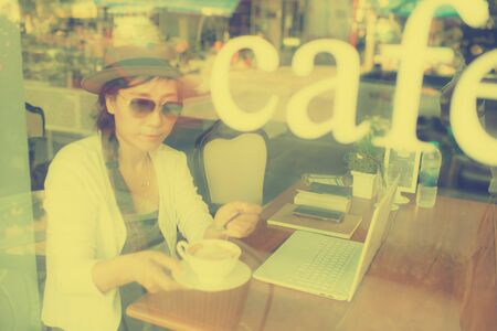 Blurry Asian woman drinking coffee and using computer in cafe.