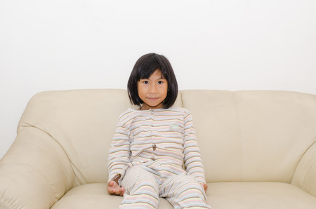 Portrait of Asian little girl sitting on sofa at home.の写真素材