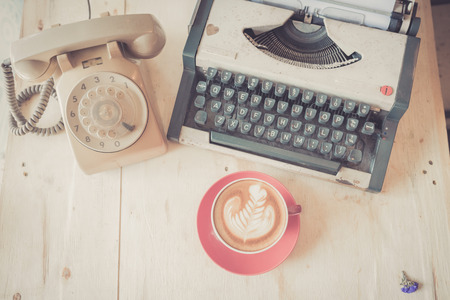 Red latte coffee cup with vintage telephone and typewriter on wooden background.の写真素材