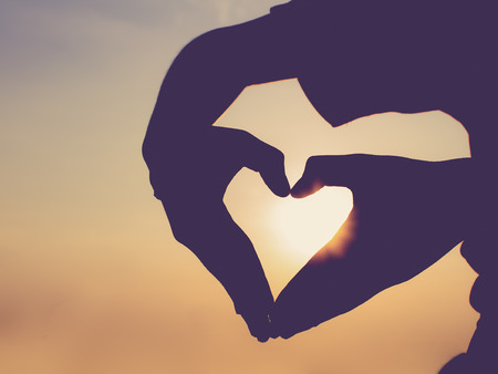 Silhouette hand in heart shape during sunset with vintage filter effect.の写真素材
