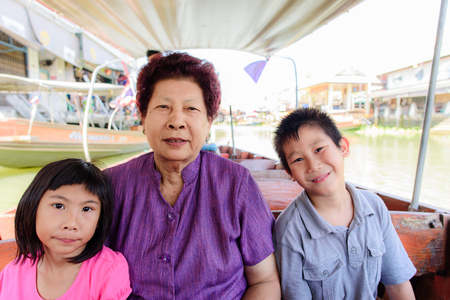 Happy Grandmother and children enjoying sightseeing long tail boat tour at floating market.の写真素材