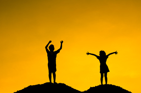 Boy and Girl raising her hands standing on top hill during sun setの写真素材