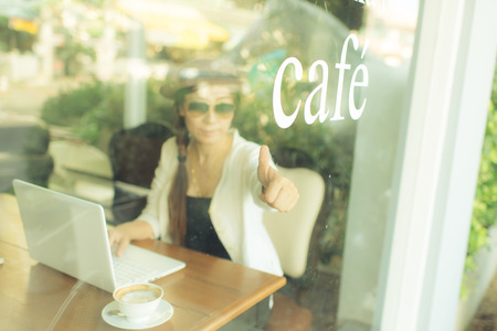 Asian woman drinking coffee and using computer in cafe. Photo filter effect.の写真素材