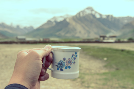 Hand holding coffee cup with Himalaya Mountain background, Rangdum, India.