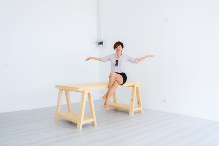Smart Asian woman sitting on big pine table in white room.の写真素材