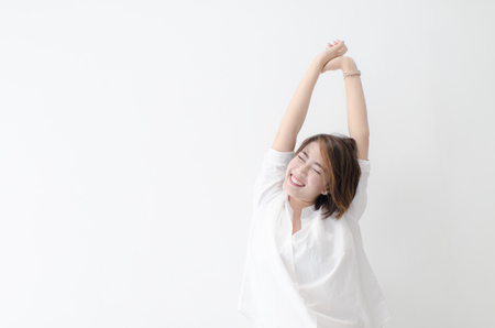 Happy Asian woman sitting on the bed, woke up and stretchedの写真素材