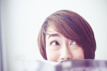 Asian woman rests at the sofa reading book,her eyes looking up something, vintage tone.の写真素材