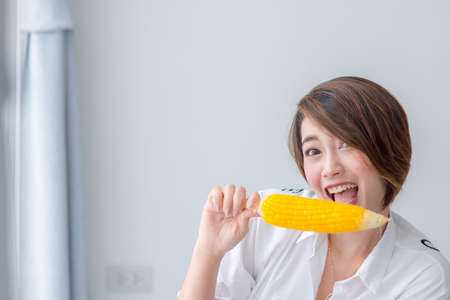 Asian girl eating yellow corn at home.の写真素材