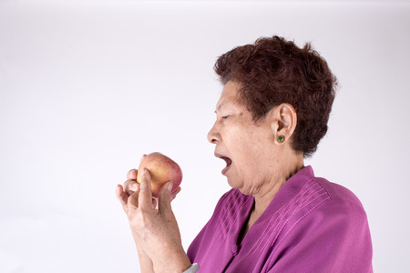Healthy lifestyle concept. Asian senior woman eating an apple over gray backgroundの写真素材
