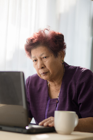 Asian senior woman learning notebook and drink a cup of tea at home.の写真素材