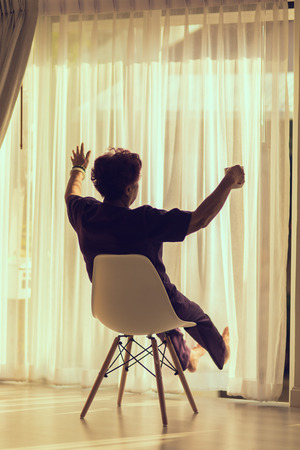 Senior woman at home sitting on modern chair in front of window relaxing in her living room room. Vintage tone.の写真素材