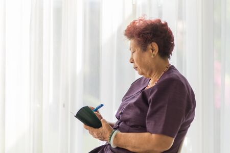Asian senior woman  with holding pencil and notebook at home.