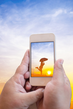 Taking pictures Children playing in sunset, silhouette, freedom and happiness with mobile phone in the blur nature backgroundの写真素材