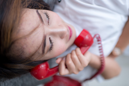 Young Asian woman laying on couch talking on red retro telephone