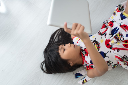 Child with tablet lying on floor. Girl playing laptop computerの写真素材