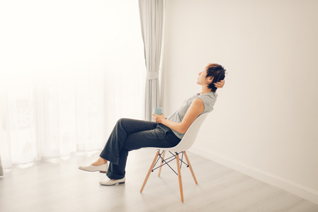 woman at home sitting on modern chair in front of window relaxing in her living room room. Vintage tone.の写真素材