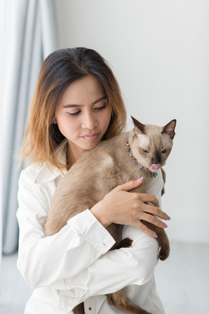 beautiful smiling Asian girl holding her cat with window light at home.の写真素材