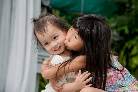 Cute Asian girl playing with her sister on bed at home.の写真素材