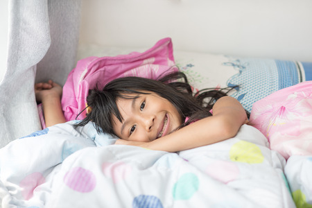 Asian girl lying under a blanket in the bed and smiling