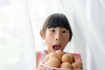 Surprising girl holding eggs bowl with white curtain
